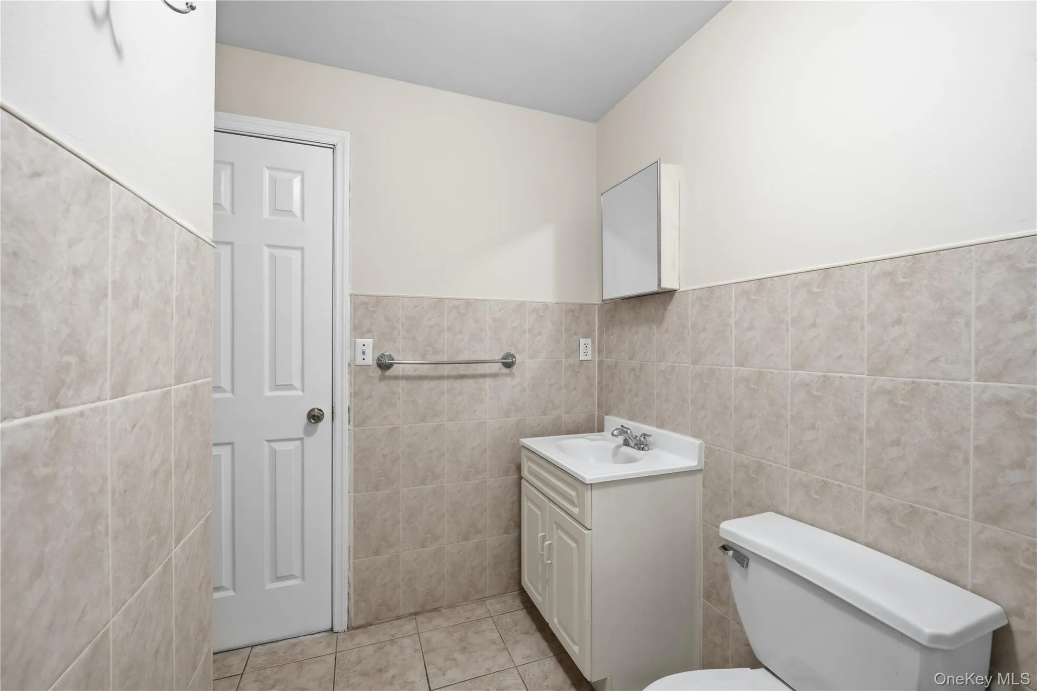 Bathroom with tile walls, vanity, wainscoting, and light tile patterned floors Bathroom with tile walls, vanity, wainscoting, and light tile patterned floors
