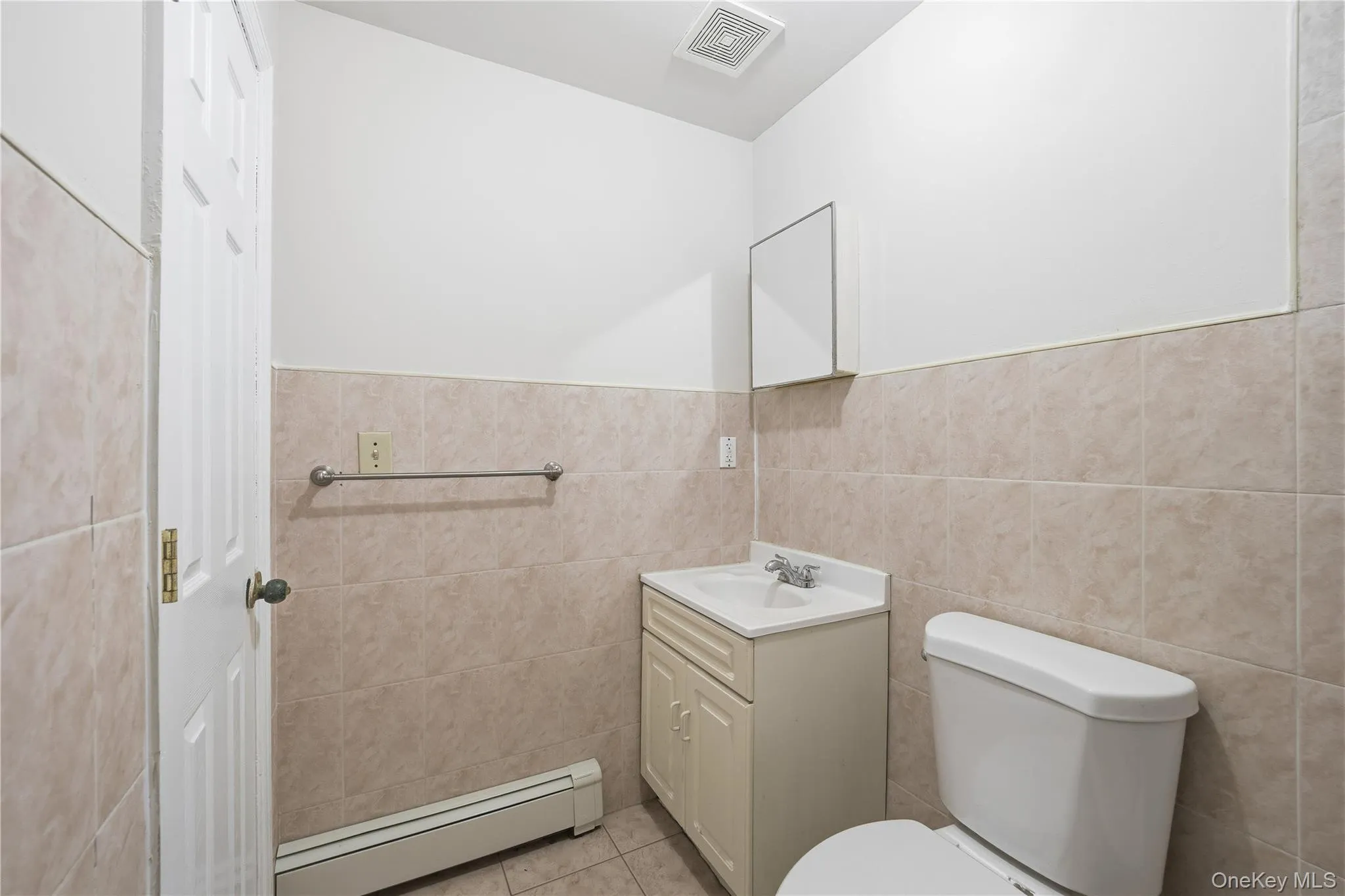 Half bath with baseboard heating, tile walls, vanity, light tile patterned floors, and wainscoting Half bath with baseboard heating, tile walls, vanity, light tile patterned floors, and wainscoting