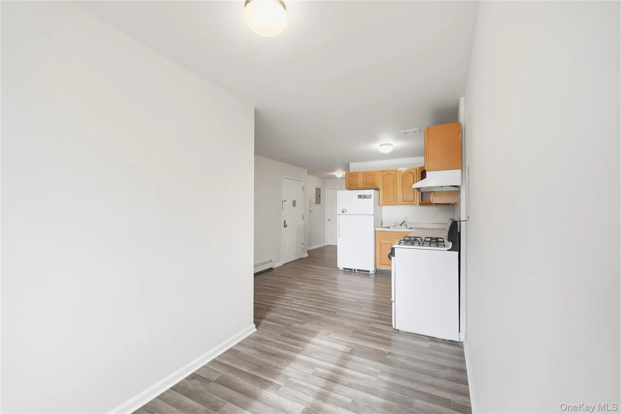 Kitchen with white appliances, light brown cabinetry, light countertops, light wood finished floors, and under cabinet range hood Kitchen with white appliances, light brown cabinetry, light countertops, light wood finished floors, and under cabinet range hood