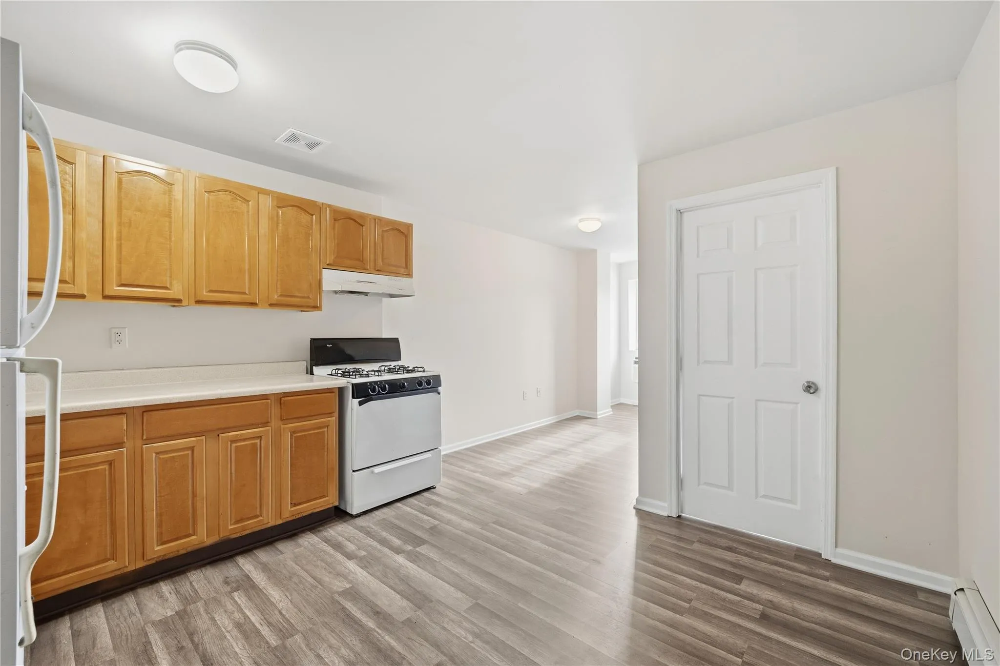 Kitchen featuring white appliances, light countertops, light wood-style flooring, baseboard heating, and under cabinet range hood Kitchen featuring white appliances, light countertops, light wood-style flooring, baseboard heating, and under cabinet range hood