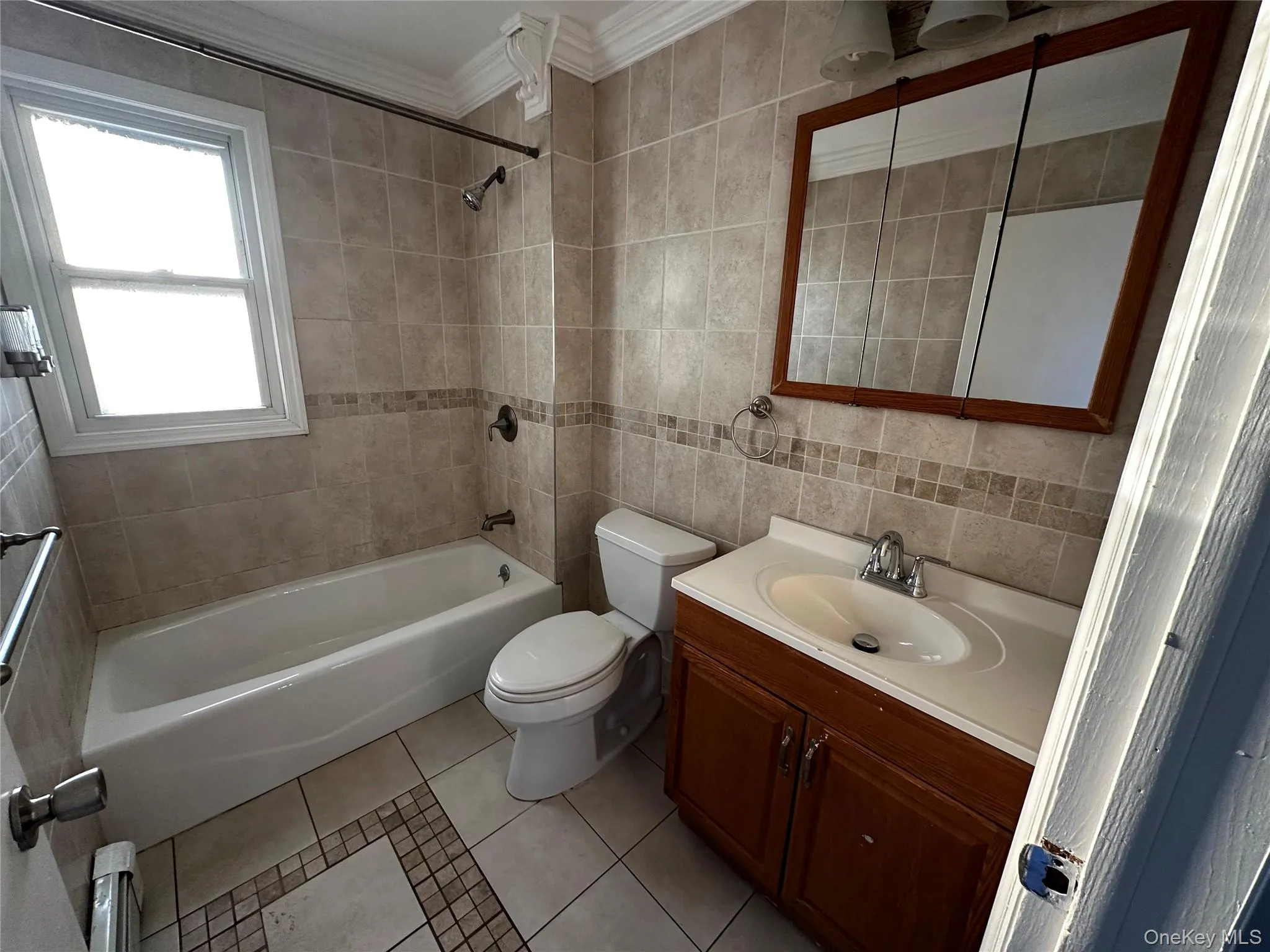 Bathroom with vanity, crown molding, light tile patterned floors, tub / shower combination, and tile walls Bathroom with vanity, crown molding, light tile patterned floors, tub / shower combination, and tile walls