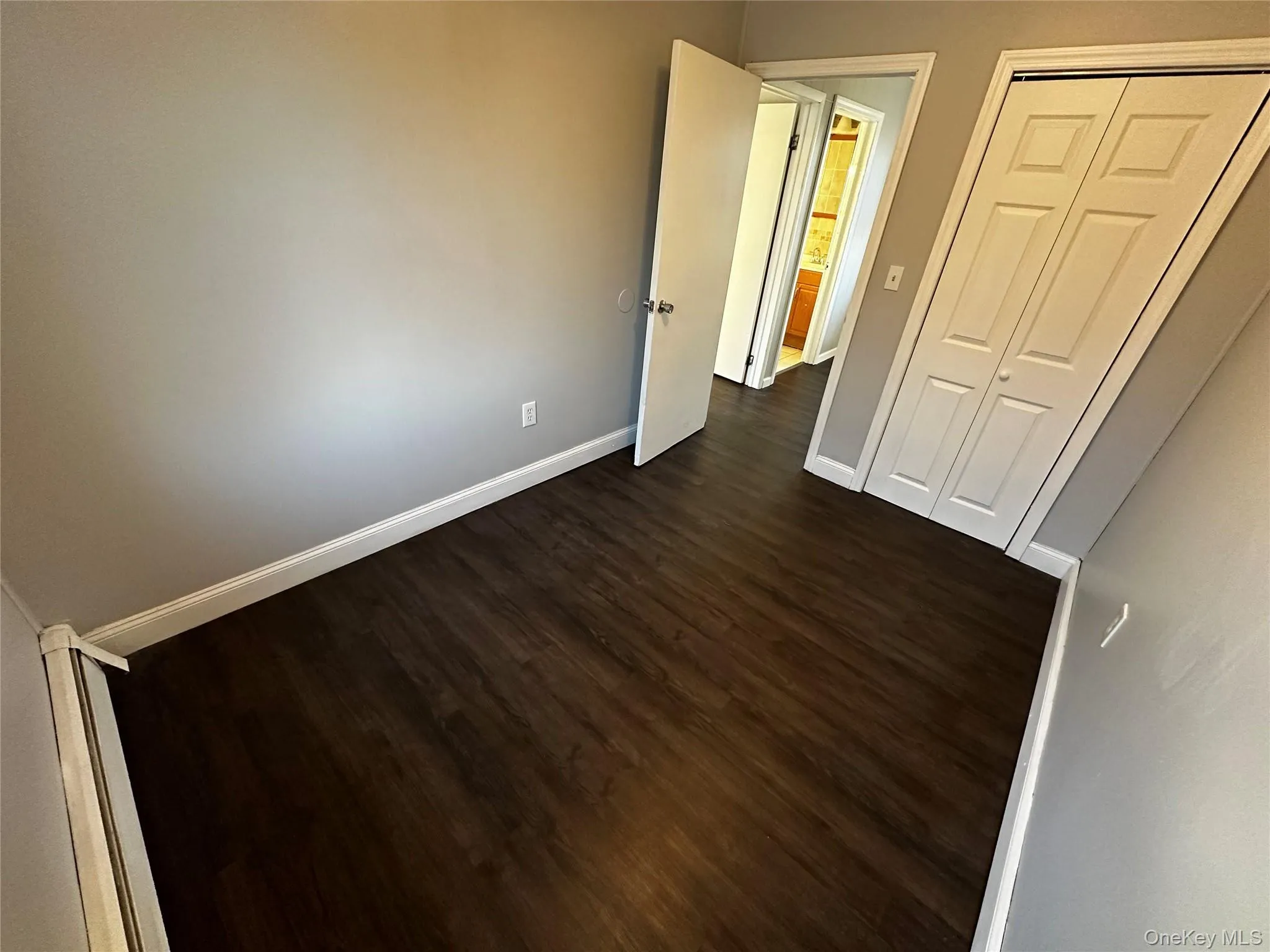Unfurnished bedroom featuring dark wood-style flooring, a closet, and a baseboard heating unit Unfurnished bedroom featuring dark wood-style flooring, a closet, and a baseboard heating unit
