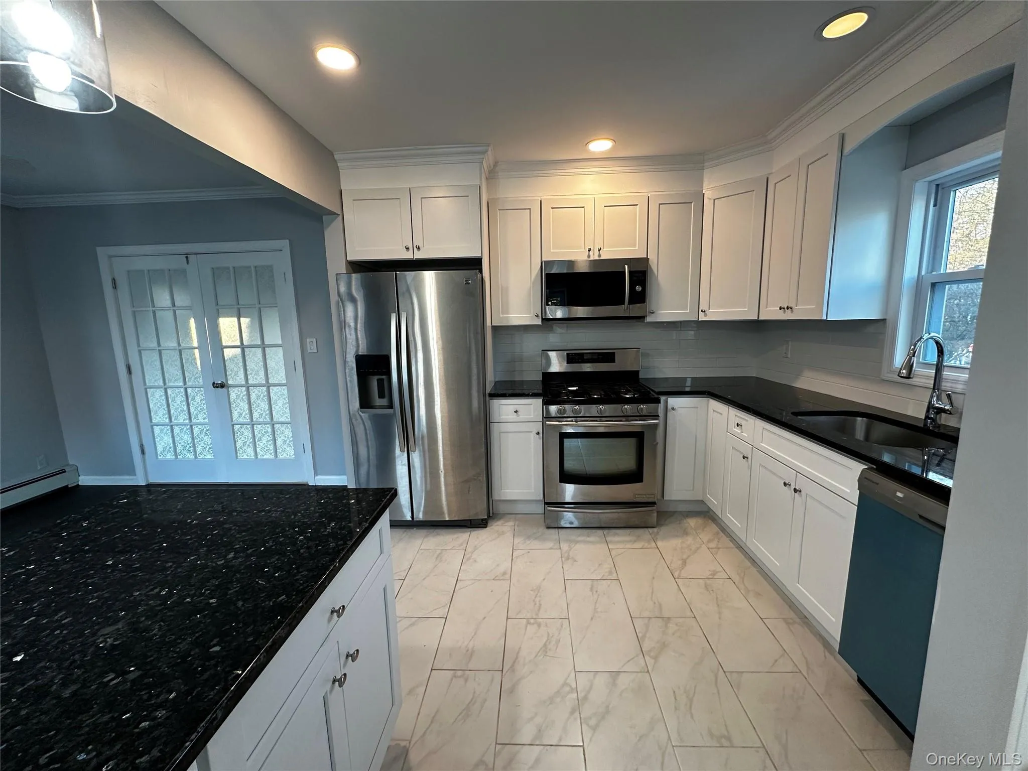 Kitchen with appliances with stainless steel finishes, white cabinetry, light marble finish floors, dark stone counters, and ornamental molding Kitchen with appliances with stainless steel finishes, white cabinetry, light marble finish floors, dark stone counters, and ornamental molding