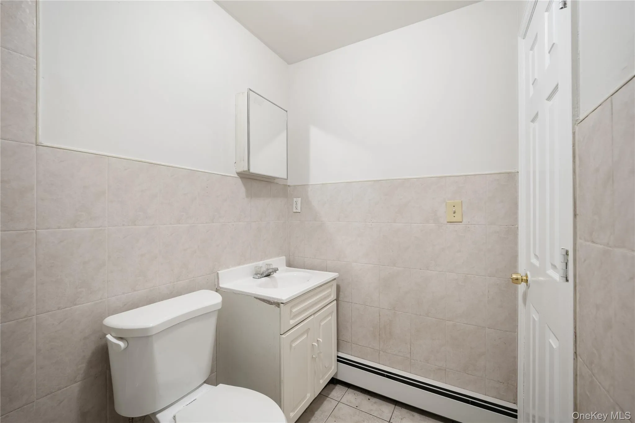 Bathroom with a baseboard heating unit, vanity, tile walls, and light tile patterned floors Bathroom with a baseboard heating unit, vanity, tile walls, and light tile patterned floors