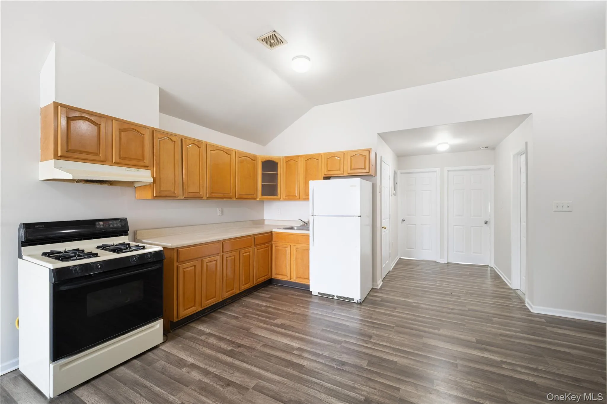 Kitchen featuring gas stove, lofted ceiling, light countertops, freestanding refrigerator, and glass insert cabinets Kitchen featuring gas stove, lofted ceiling, light countertops, freestanding refrigerator, and glass insert cabinets