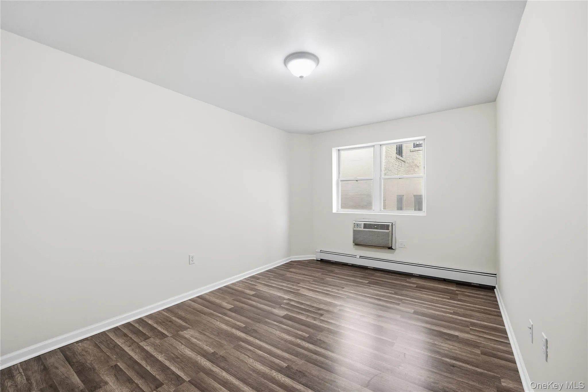 Spare room featuring a baseboard heating unit, dark wood-type flooring, and a wall unit AC Spare room featuring a baseboard heating unit, dark wood-type flooring, and a wall unit AC