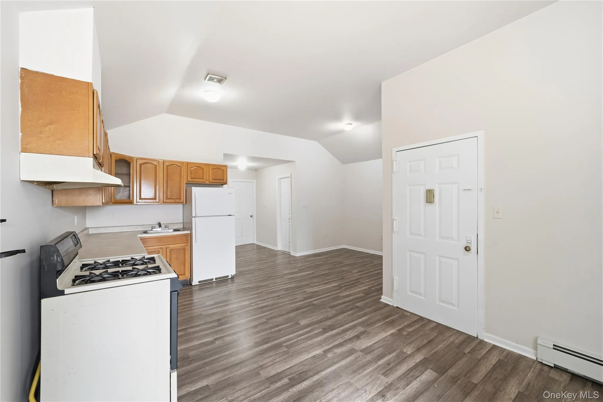 Kitchen featuring white appliances, light countertops, under cabinet range hood, lofted ceiling, and a baseboard heating unit Kitchen featuring white appliances, light countertops, under cabinet range hood, lofted ceiling, and a baseboard heating unit