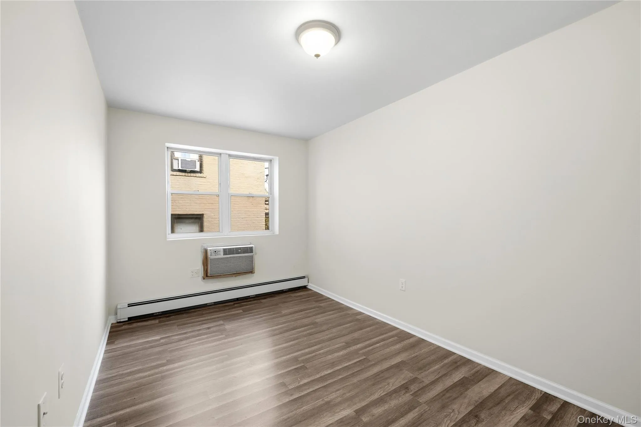 Empty room featuring a baseboard radiator, wood finished floors, and a wall mounted air conditioner Empty room featuring a baseboard radiator, wood finished floors, and a wall mounted air conditioner