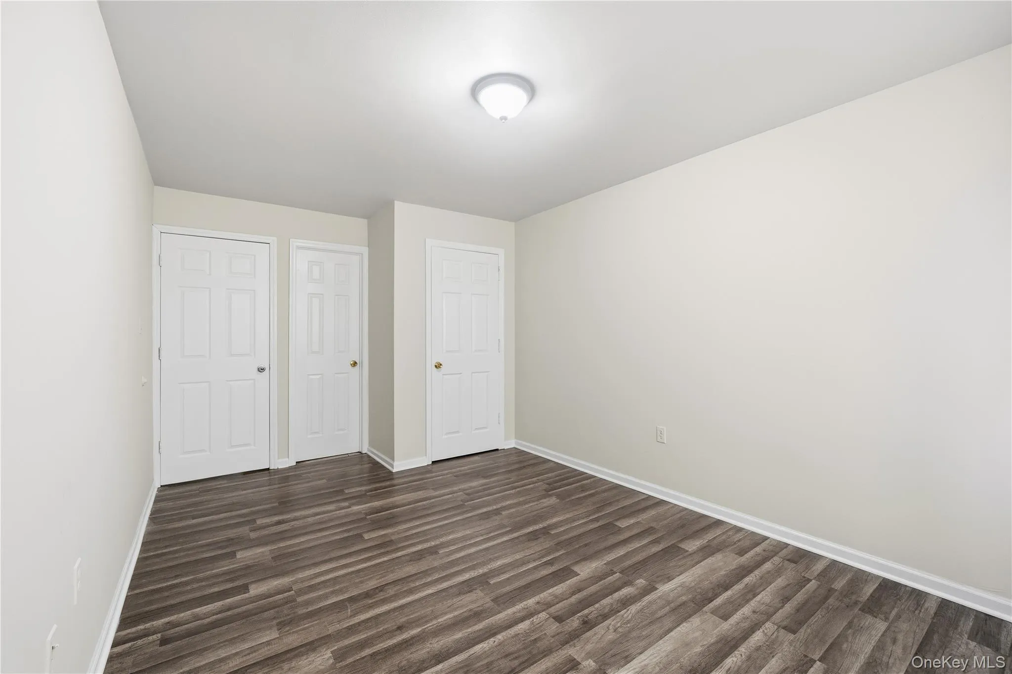Unfurnished bedroom with dark wood-type flooring and baseboards Unfurnished bedroom with dark wood-type flooring and baseboards