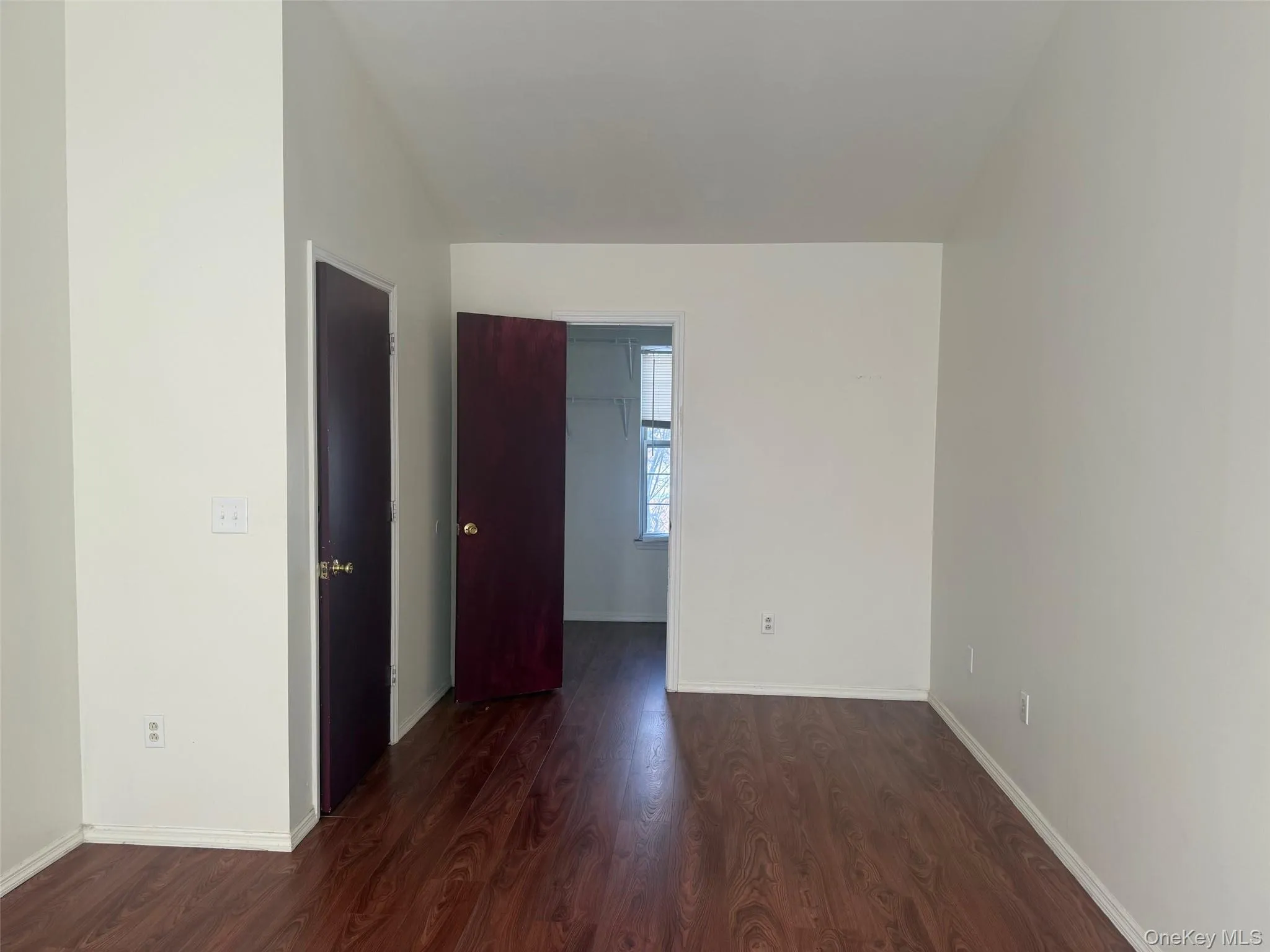 Empty room with dark wood-type flooring and baseboards Empty room with dark wood-type flooring and baseboards