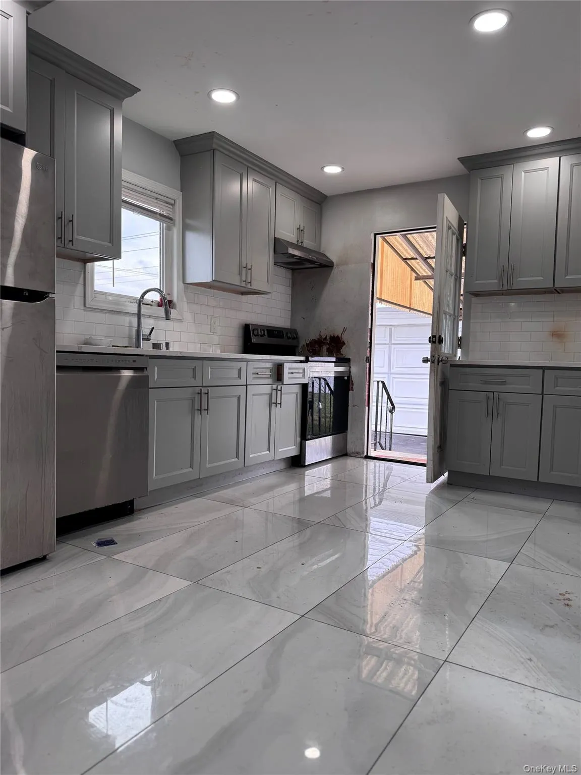 Kitchen with gray cabinets, light marble finish floors, stainless steel appliances, under cabinet range hood, and decorative backsplash Kitchen with gray cabinets, light marble finish floors, stainless steel appliances, under cabinet range hood, and decorative backsplash