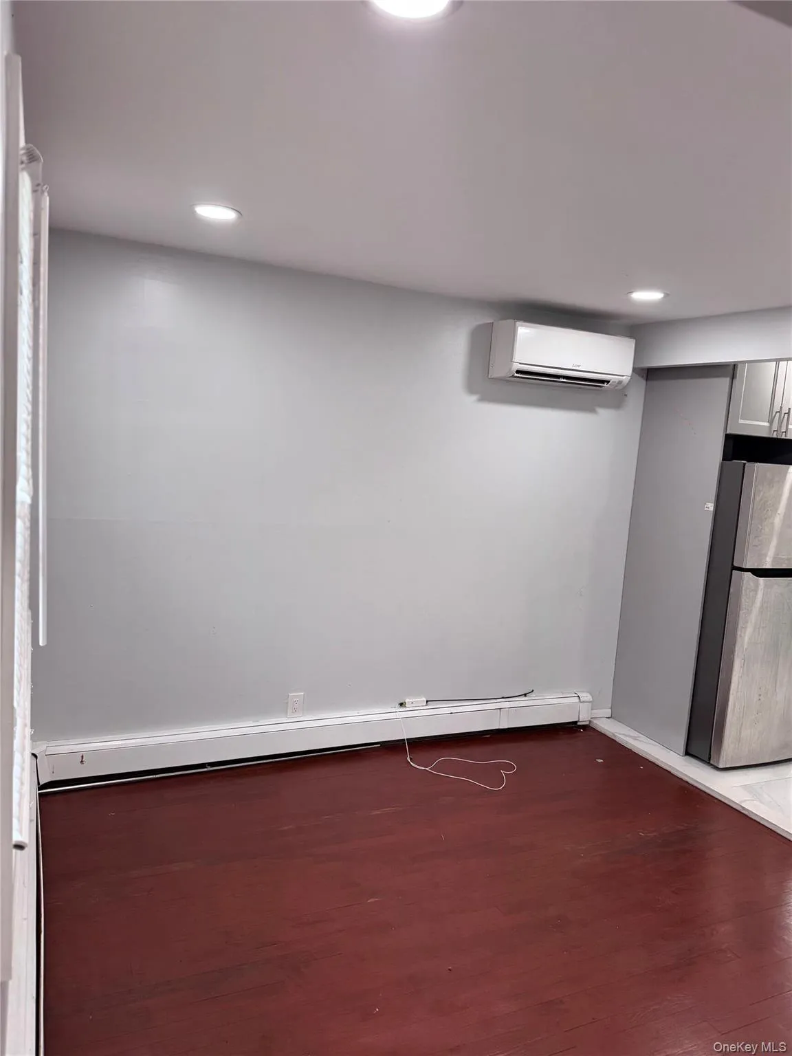 Finished basement featuring freestanding refrigerator, a baseboard heating unit, dark wood-style floors, recessed lighting, and a wall mounted AC Finished basement featuring freestanding refrigerator, a baseboard heating unit, dark wood-style floors, recessed lighting, and a wall mounted AC