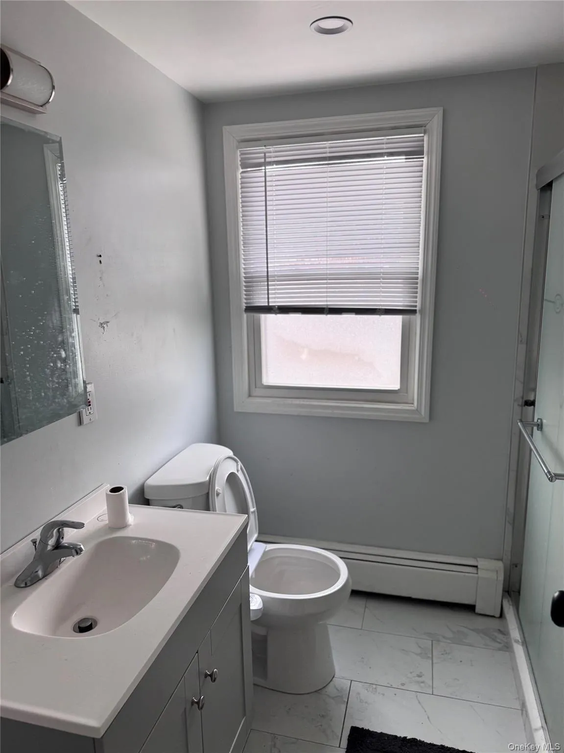 Bathroom with light marble finish flooring, vanity, a shower stall, and a baseboard radiator Bathroom with light marble finish flooring, vanity, a shower stall, and a baseboard radiator