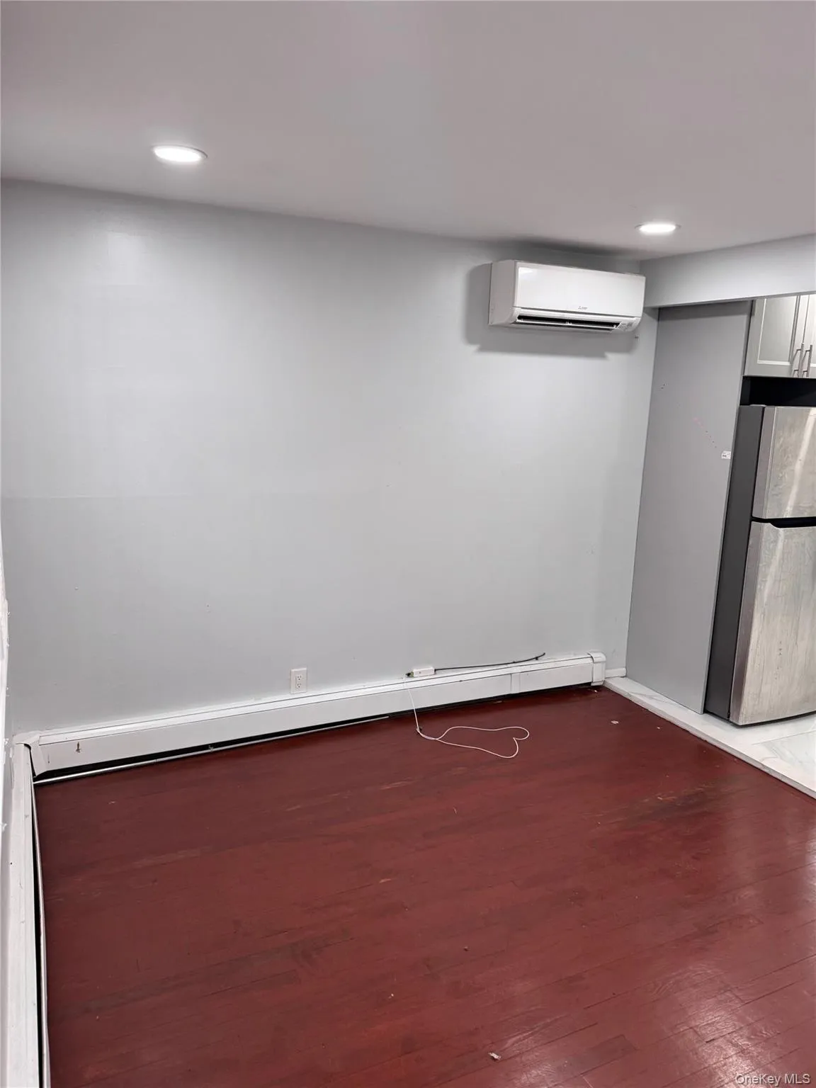 Finished below grade area featuring freestanding refrigerator, dark wood-type flooring, a baseboard radiator, an AC wall unit, and recessed lighting Finished below grade area featuring freestanding refrigerator, dark wood-type flooring, a baseboard radiator, an AC wall unit, and recessed lighting