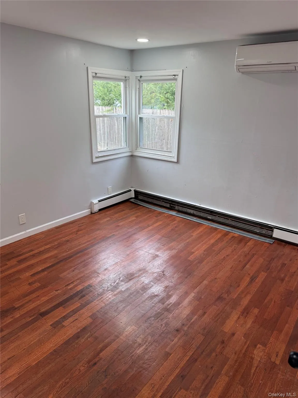 Unfurnished room featuring baseboard heating, dark wood finished floors, and a wall unit AC Unfurnished room featuring baseboard heating, dark wood finished floors, and a wall unit AC