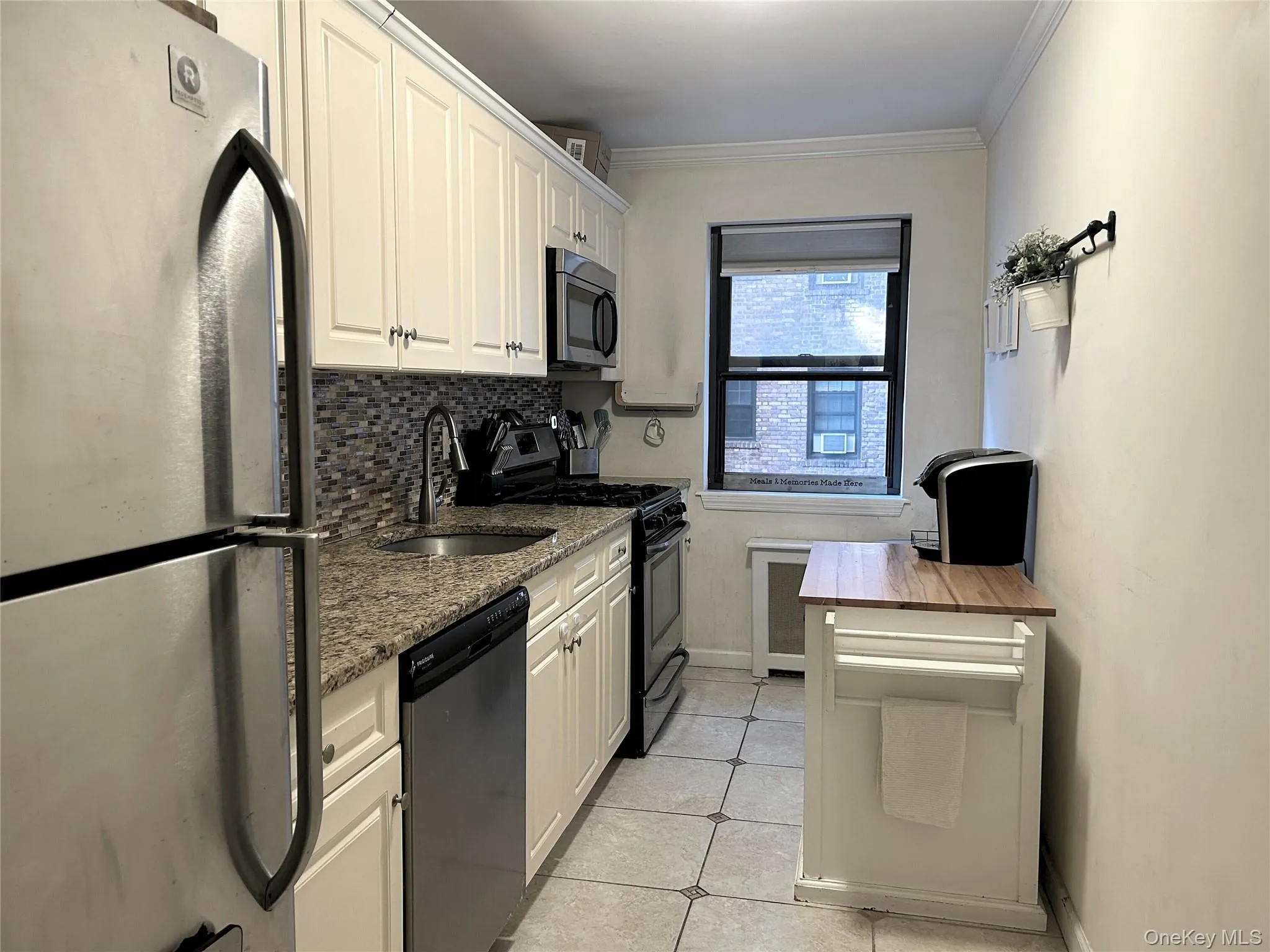Kitchen with appliances with stainless steel finishes, dark stone counters, light tile patterned flooring, tasteful backsplash, and crown molding Kitchen with appliances with stainless steel finishes, dark stone counters, light tile patterned flooring, tasteful backsplash, and crown molding