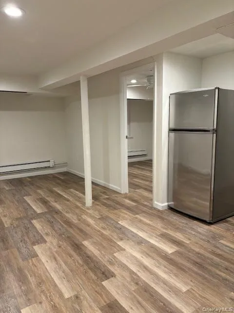 Finished below grade area featuring freestanding refrigerator, recessed lighting, light wood-type flooring, and a baseboard heating unit Finished below grade area featuring freestanding refrigerator, recessed lighting, light wood-type flooring, and a baseboard heating unit
