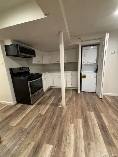 Kitchen with gas range, stacked washer and clothes dryer, white cabinetry, light countertops, and light wood-style flooring Kitchen with gas range, stacked washer and clothes dryer, white cabinetry, light countertops, and light wood-style flooring