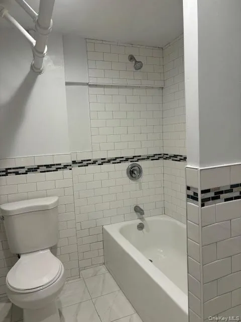 Full bathroom with tile walls, tub / shower combination, and a wainscoted wall Full bathroom with tile walls, tub / shower combination, and a wainscoted wall