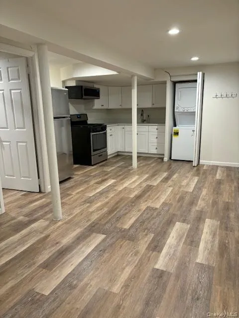 Kitchen with appliances with stainless steel finishes, stacked washer / dryer, white cabinets, light wood-type flooring, and recessed lighting Kitchen with appliances with stainless steel finishes, stacked washer / dryer, white cabinets, light wood-type flooring, and recessed lighting