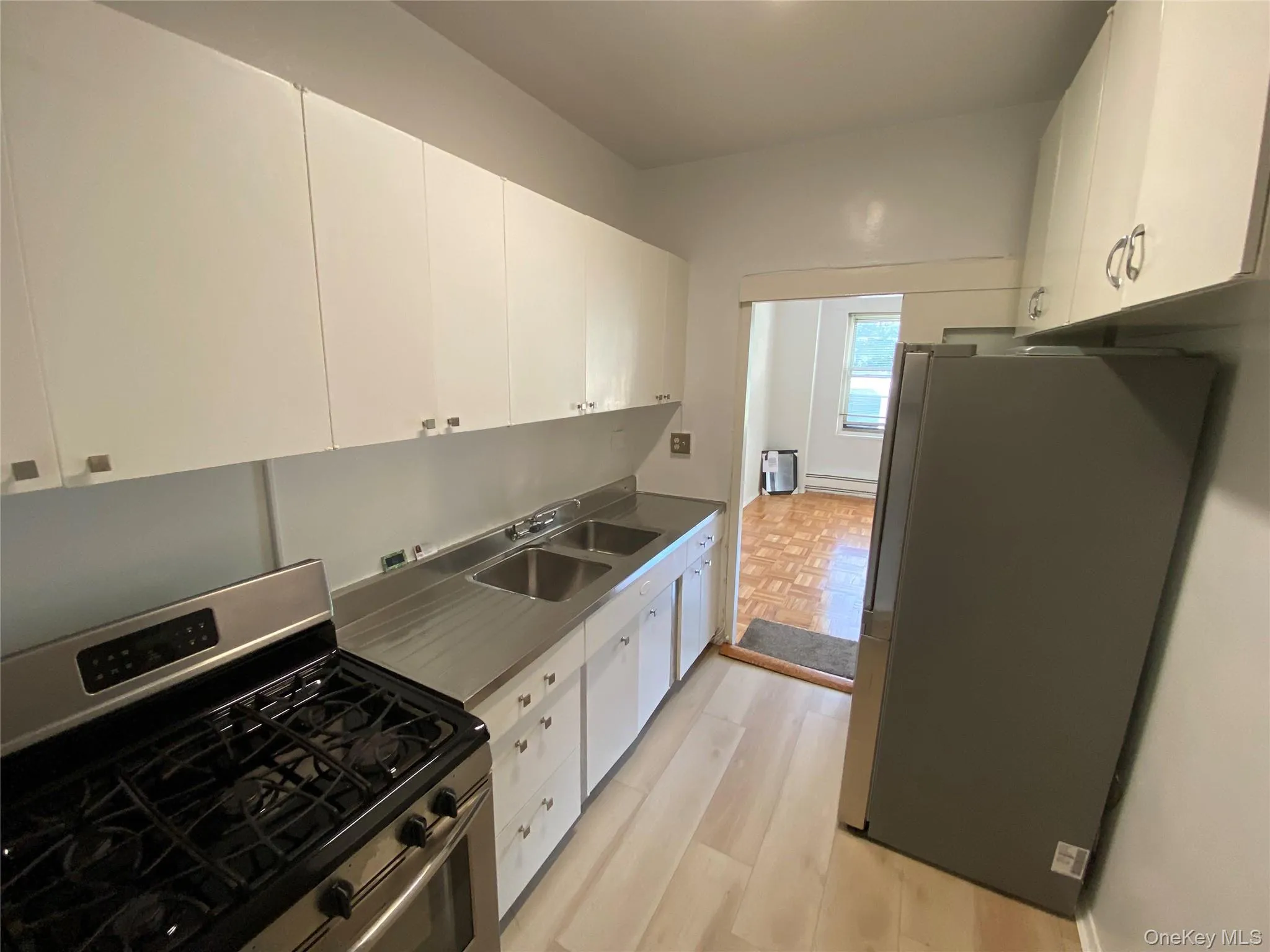 Kitchen featuring stainless steel appliances, white cabinets, light wood-style flooring, and stainless steel counters Kitchen featuring stainless steel appliances, white cabinets, light wood-style flooring, and stainless steel counters