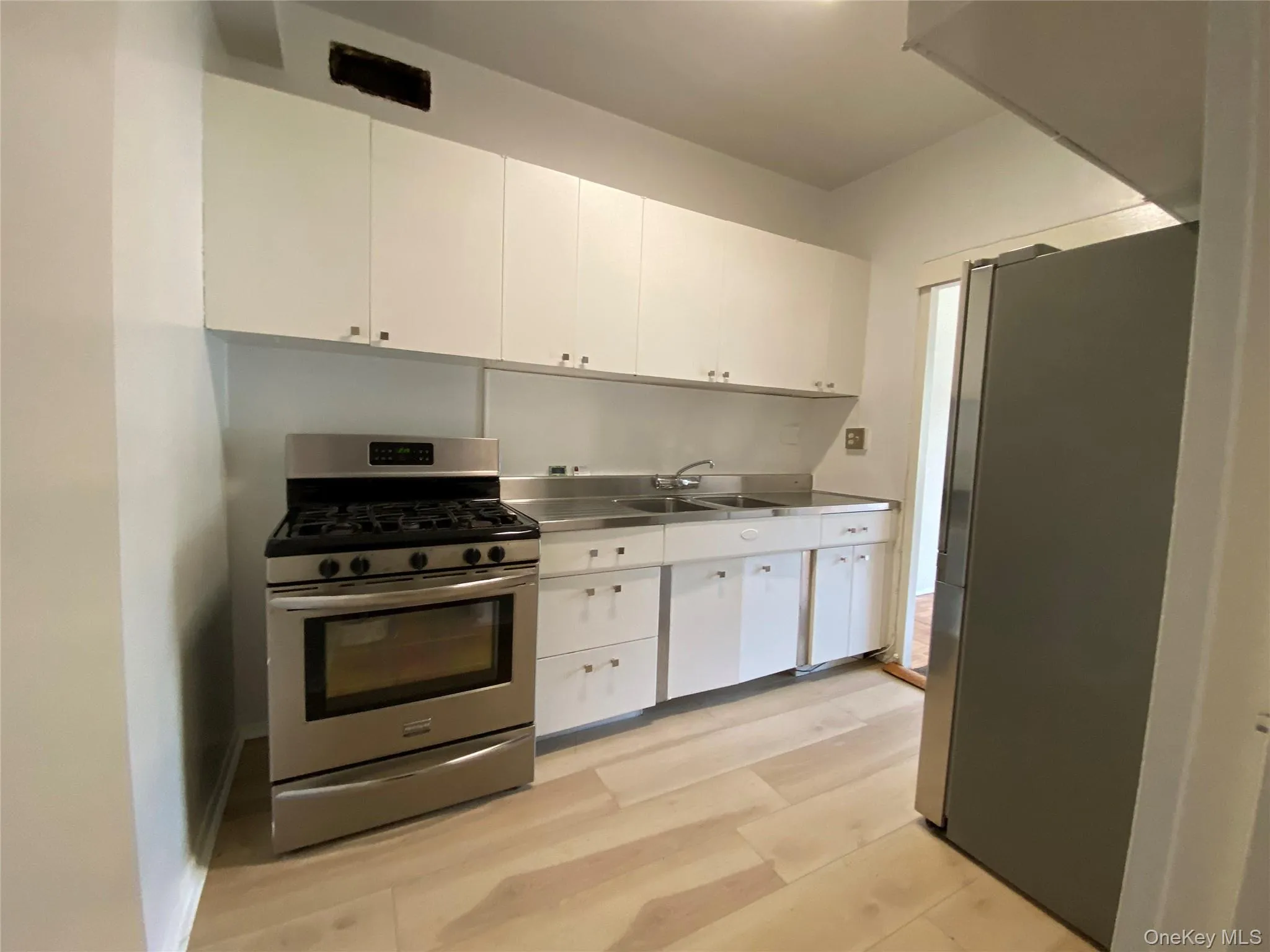 Kitchen featuring stainless steel counters, appliances with stainless steel finishes, white cabinets, and light wood-style floors Kitchen featuring stainless steel counters, appliances with stainless steel finishes, white cabinets, and light wood-style floors