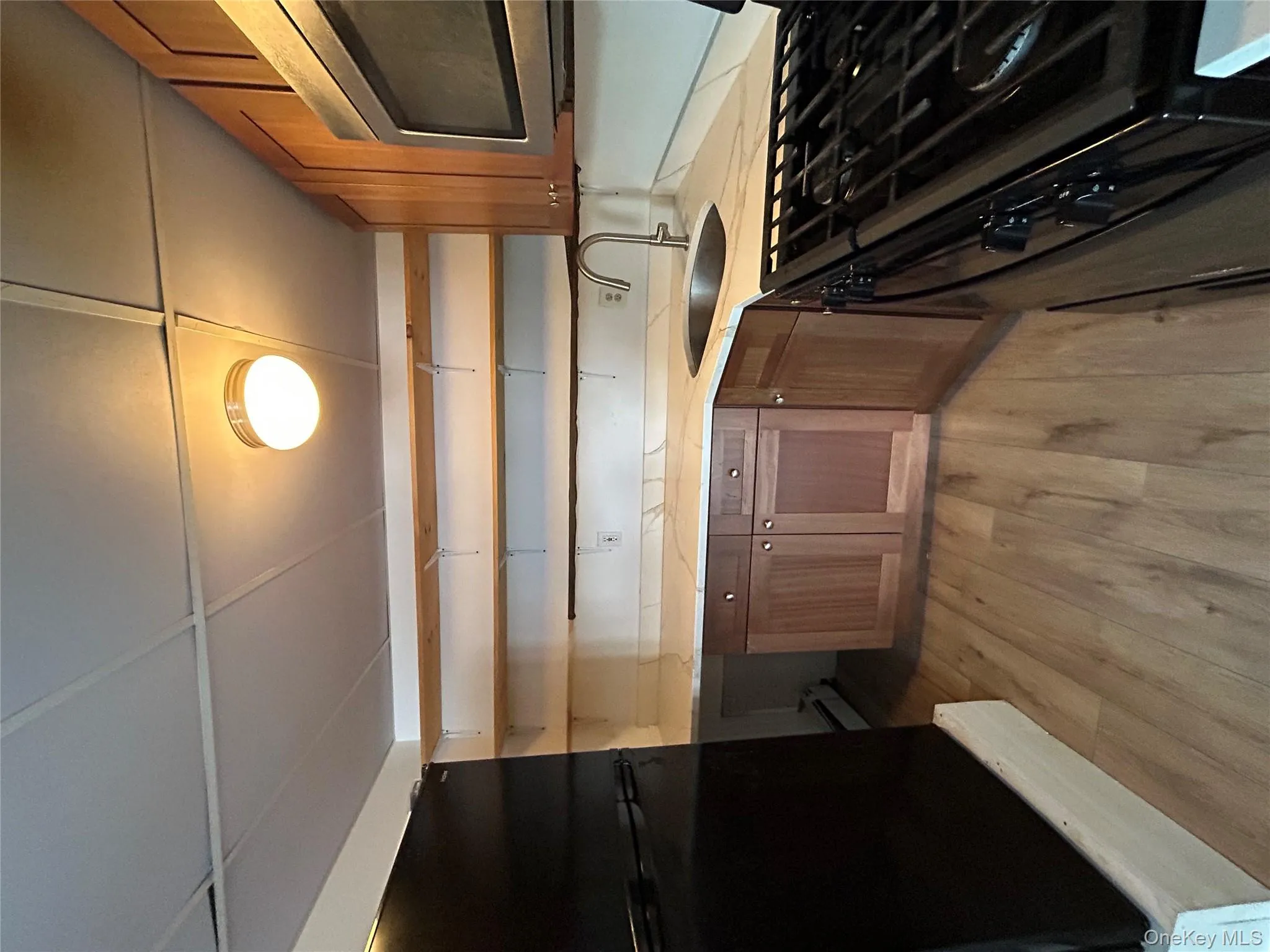 Kitchen featuring open shelves, range, brown cabinetry, black microwave, and light wood-type flooring Kitchen featuring open shelves, range, brown cabinetry, black microwave, and light wood-type flooring