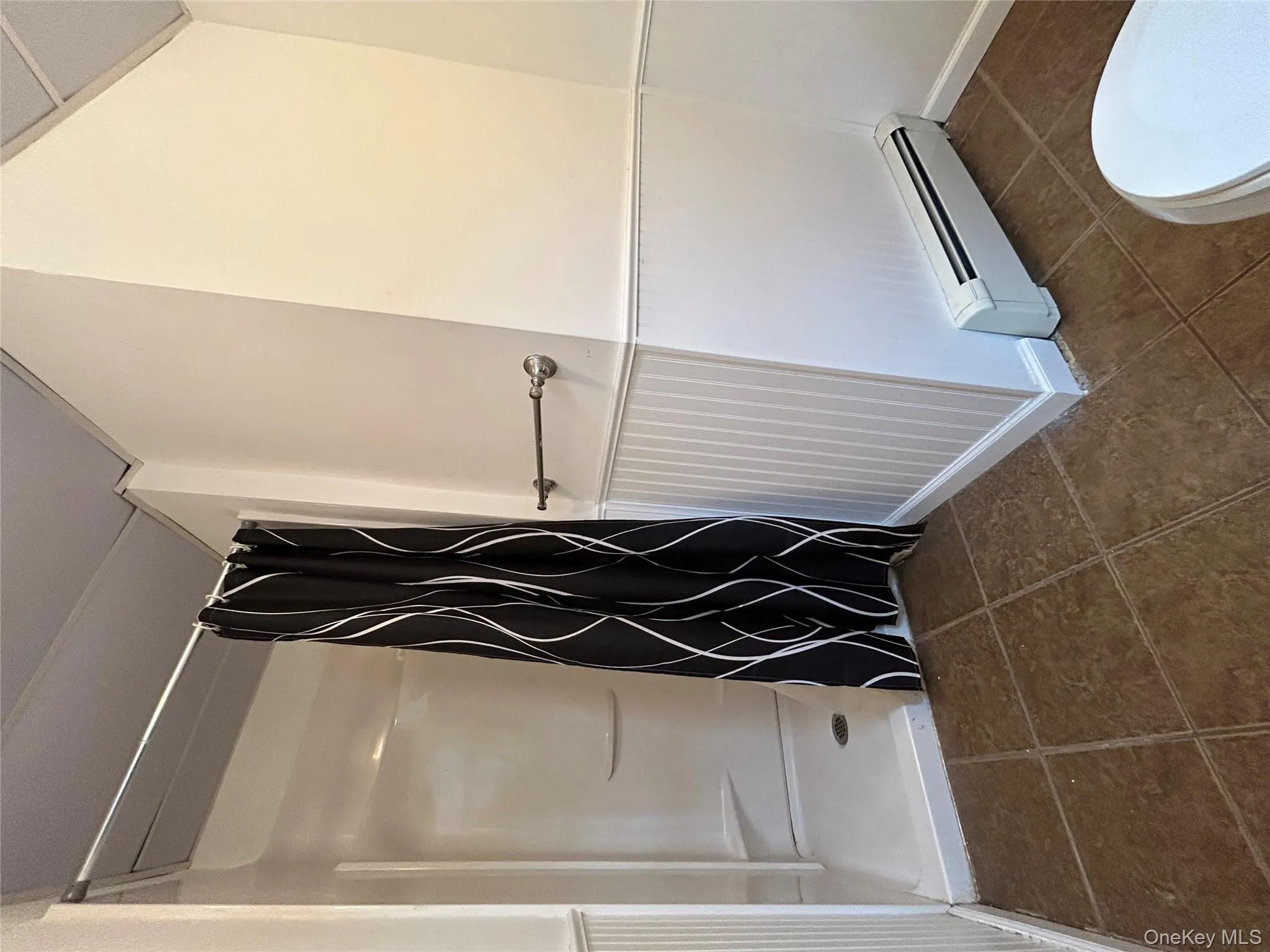 Bathroom featuring baseboard heating, a stall shower, dark tile patterned floors, and wainscoting Bathroom featuring baseboard heating, a stall shower, dark tile patterned floors, and wainscoting