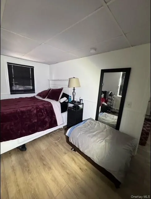 Bedroom featuring wood finished floors, a paneled ceiling, and wainscoting Bedroom featuring wood finished floors, a paneled ceiling, and wainscoting