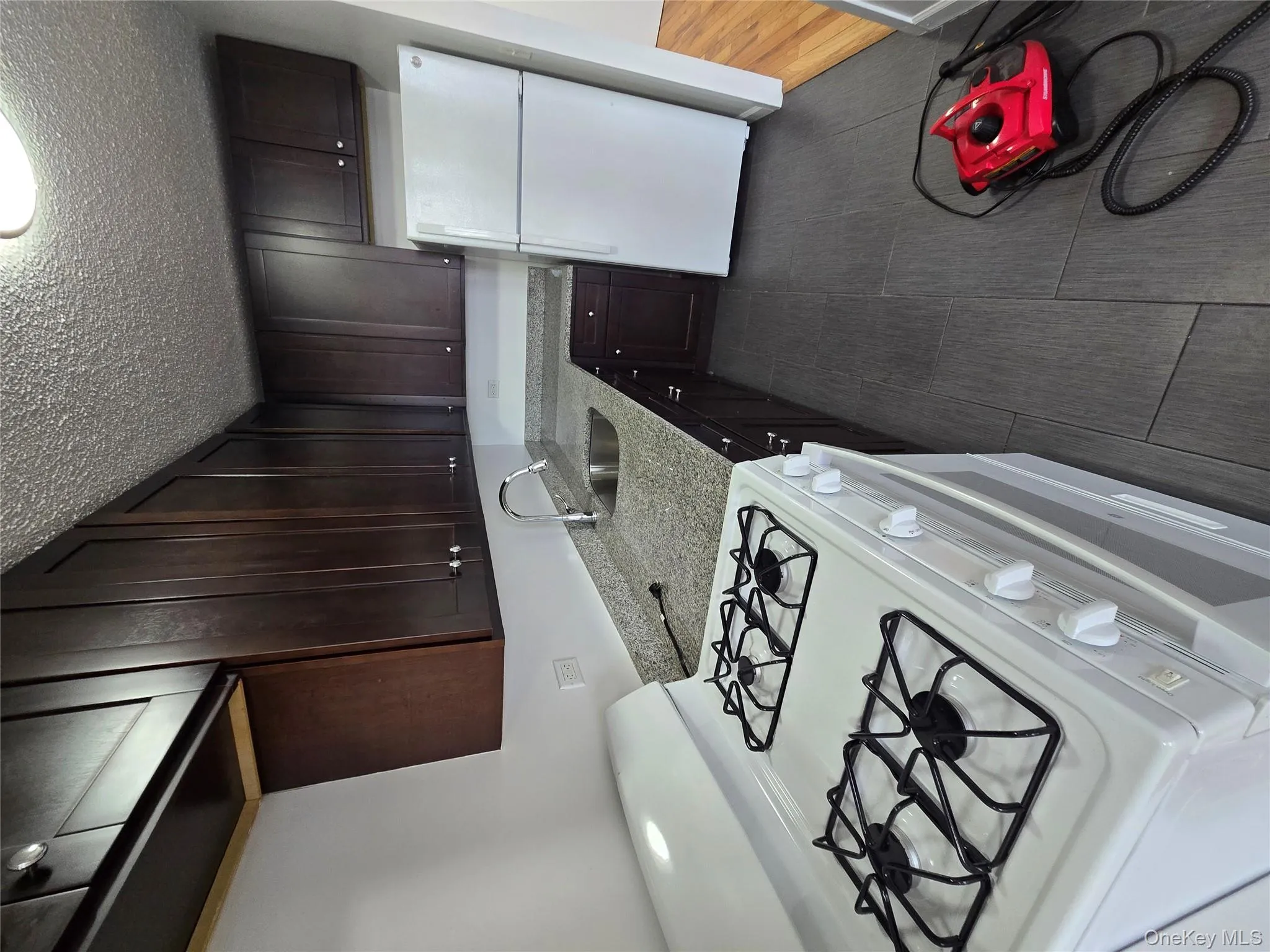 Kitchen featuring stove, white fridge, dark brown cabinetry, light stone counters, and a textured ceiling Kitchen featuring stove, white fridge, dark brown cabinetry, light stone counters, and a textured ceiling
