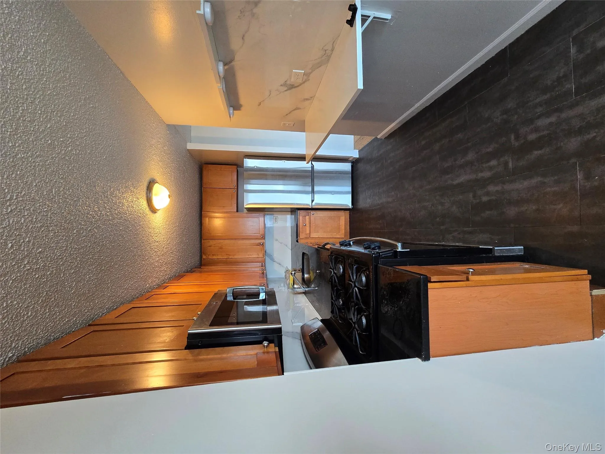 Kitchen with stainless steel range oven, refrigerator, brown cabinetry, dark wood-type flooring, and dark stone countertops Kitchen with stainless steel range oven, refrigerator, brown cabinetry, dark wood-type flooring, and dark stone countertops