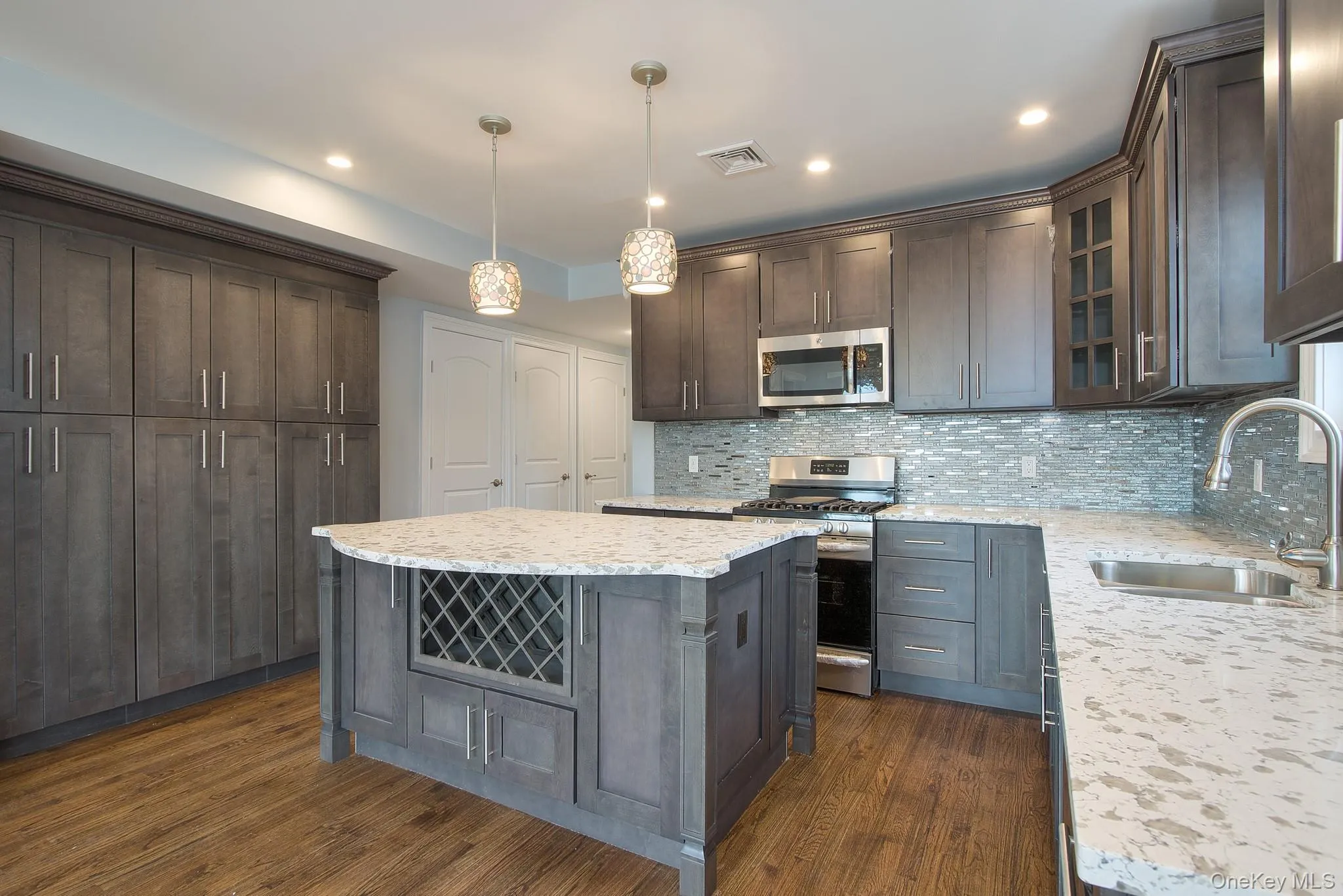 Kitchen featuring dark brown cabinetry, appliances with stainless steel finishes, pendant lighting, glass insert cabinets, and a center island Kitchen featuring dark brown cabinetry, appliances with stainless steel finishes, pendant lighting, glass insert cabinets, and a center island