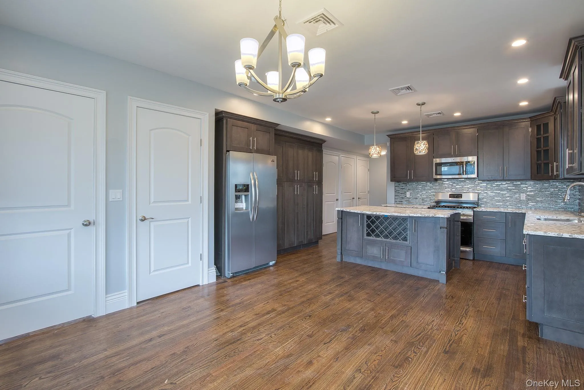 Kitchen featuring decorative light fixtures, appliances with stainless steel finishes, dark brown cabinets, light stone countertops, and a center island Kitchen featuring decorative light fixtures, appliances with stainless steel finishes, dark brown cabinets, light stone countertops, and a center island