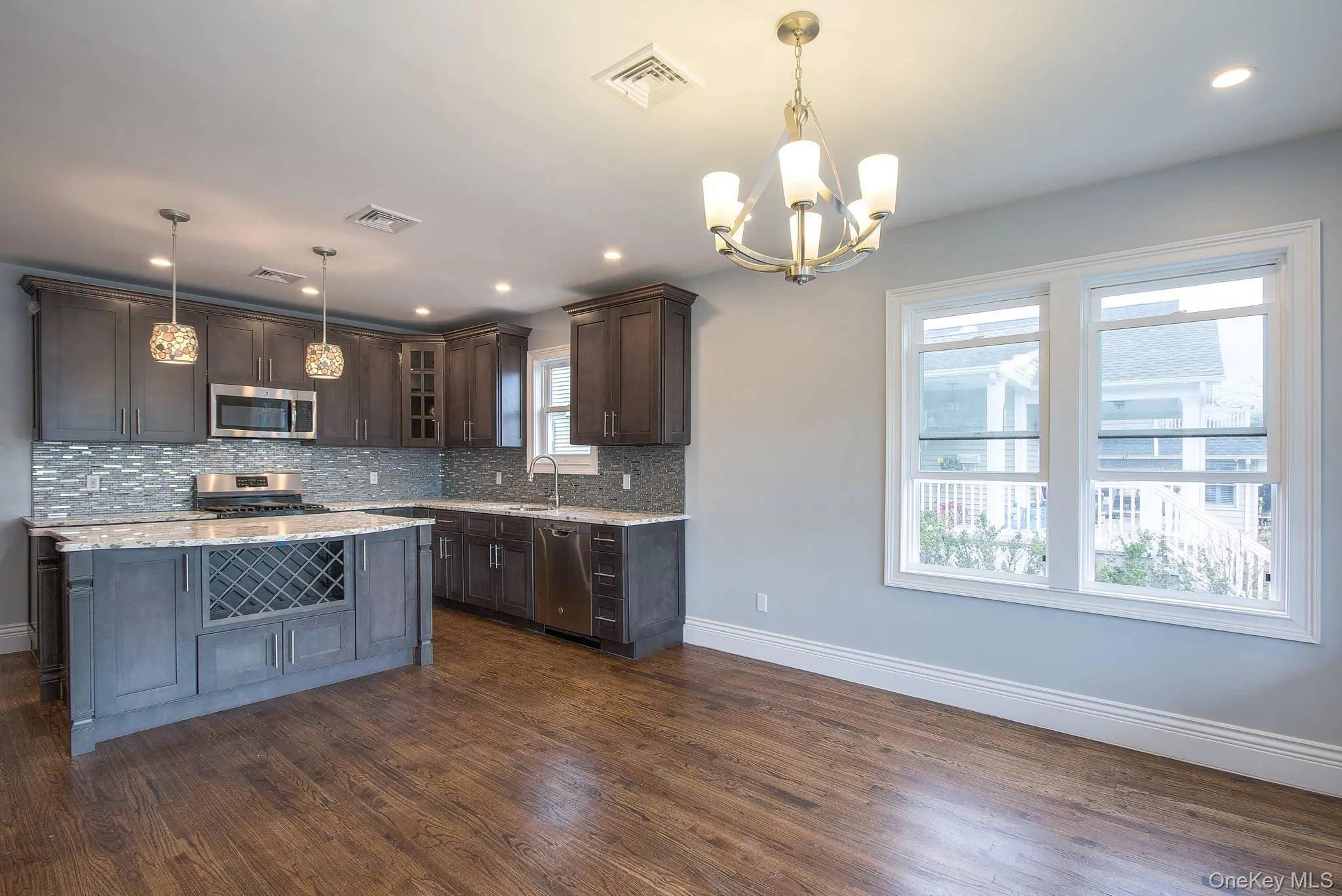 Kitchen featuring glass insert cabinets, dark brown cabinetry, appliances with stainless steel finishes, decorative light fixtures, and light stone counters Kitchen featuring glass insert cabinets, dark brown cabinetry, appliances with stainless steel finishes, decorative light fixtures, and light stone counters