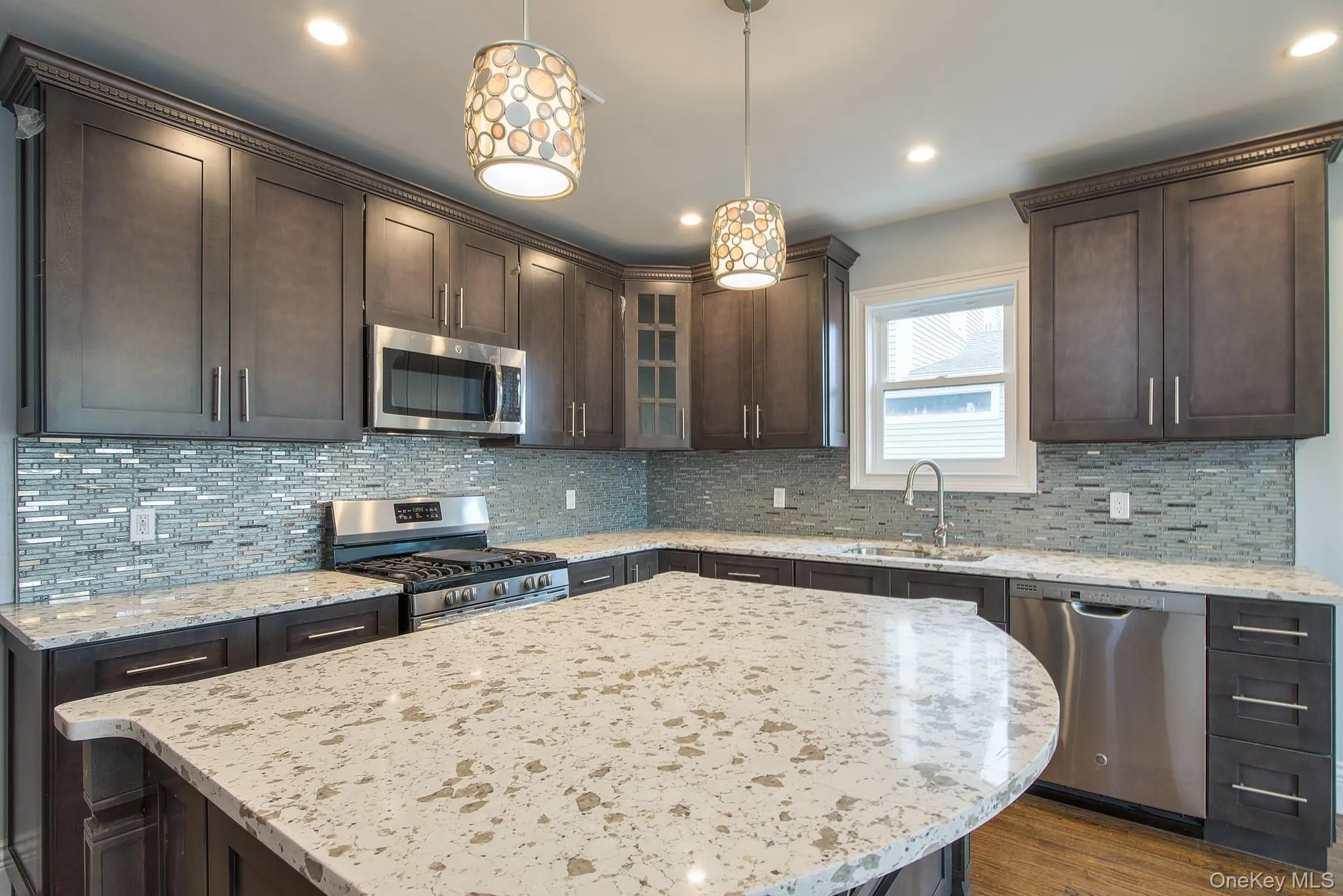 Kitchen featuring dark brown cabinets, appliances with stainless steel finishes, light stone counters, decorative light fixtures, and recessed lighting Kitchen featuring dark brown cabinets, appliances with stainless steel finishes, light stone counters, decorative light fixtures, and recessed lighting