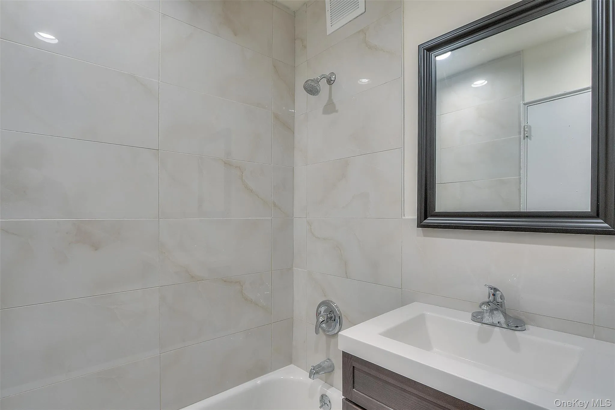 Bathroom with tub / shower combination, vanity, and tile walls Bathroom with tub / shower combination, vanity, and tile walls