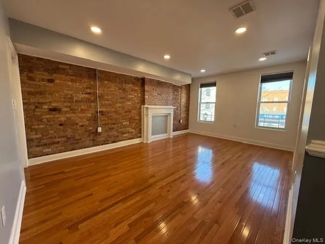 Unfurnished living room with hardwood / wood-style flooring, brick wall, a fireplace, and recessed lighting Unfurnished living room with hardwood / wood-style flooring, brick wall, a fireplace, and recessed lighting