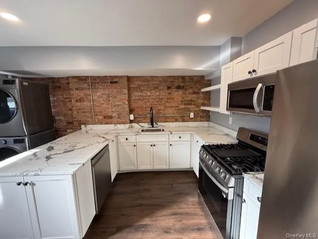 Kitchen with stainless steel appliances, a peninsula, white cabinetry, brick wall, and dark wood finished floors Kitchen with stainless steel appliances, a peninsula, white cabinetry, brick wall, and dark wood finished floors