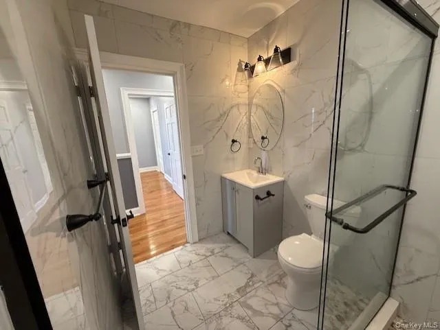 Full bathroom with stone wall, light marble finish flooring, tile walls, vanity, and a marble finish shower Full bathroom with stone wall, light marble finish flooring, tile walls, vanity, and a marble finish shower