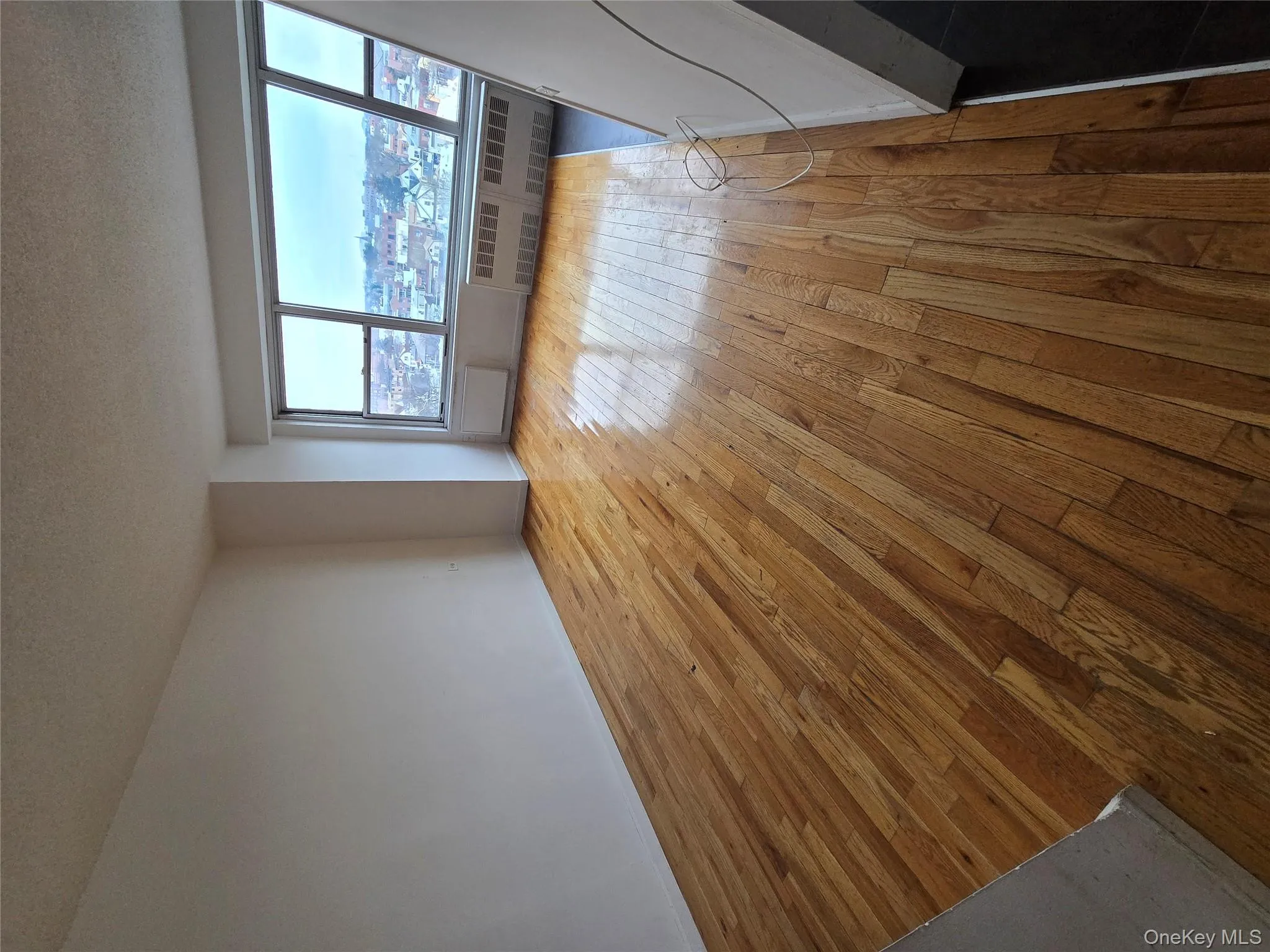 Unfurnished room with light wood finished floors, a textured ceiling, a view of city, and radiator Unfurnished room with light wood finished floors, a textured ceiling, a view of city, and radiator