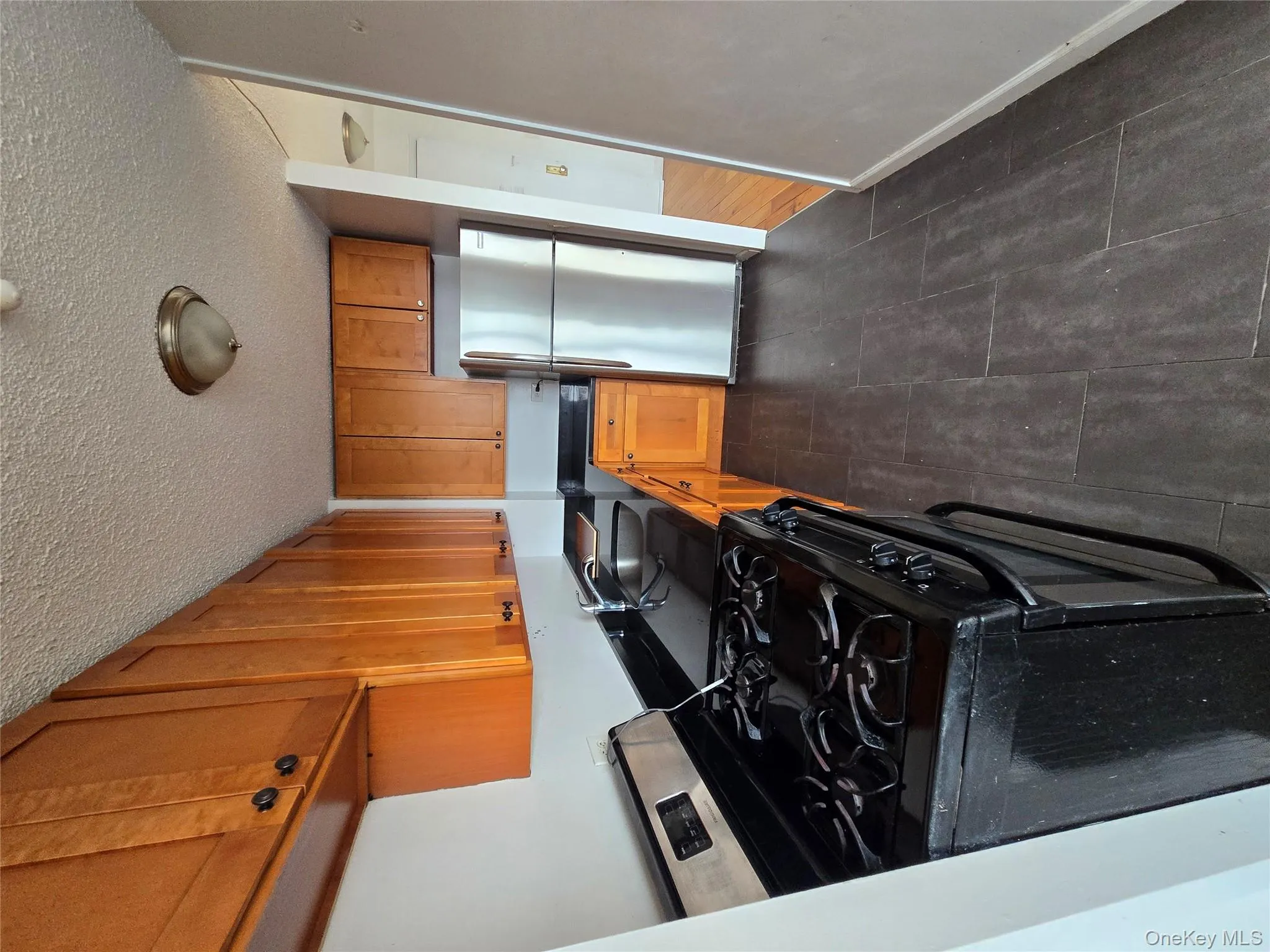 Kitchen with range, black fridge, brown cabinetry, a textured ceiling, and dark tile patterned floors Kitchen with range, black fridge, brown cabinetry, a textured ceiling, and dark tile patterned floors