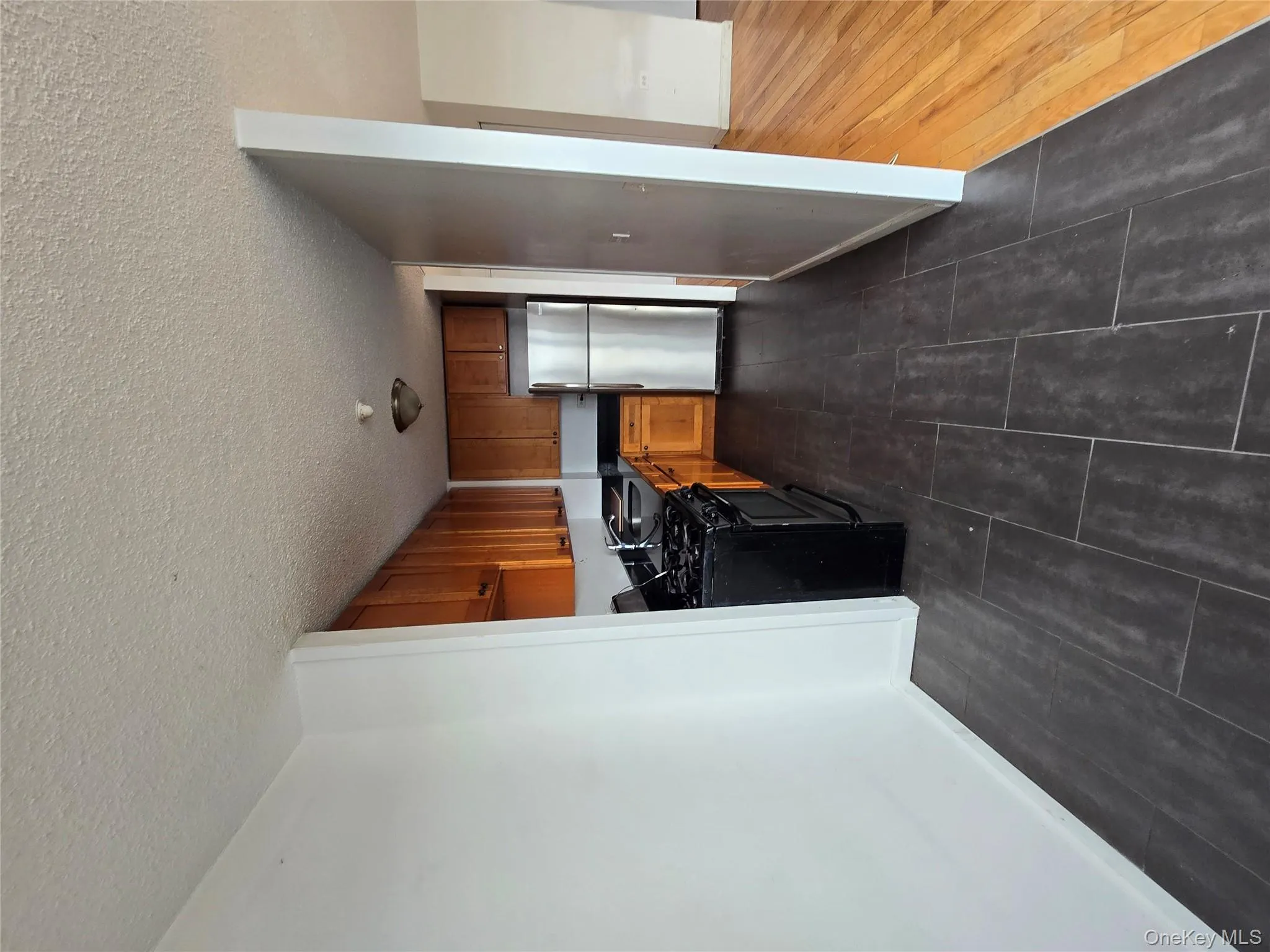 Kitchen with stove, dark countertops, black fridge, a textured ceiling, and brown cabinets Kitchen with stove, dark countertops, black fridge, a textured ceiling, and brown cabinets
