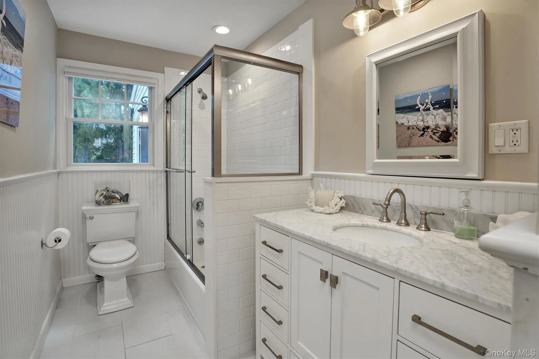 Bathroom featuring wainscoting, light tile patterned floors, vanity, and enclosed tub / shower combo Bathroom featuring wainscoting, light tile patterned floors, vanity, and enclosed tub / shower combo