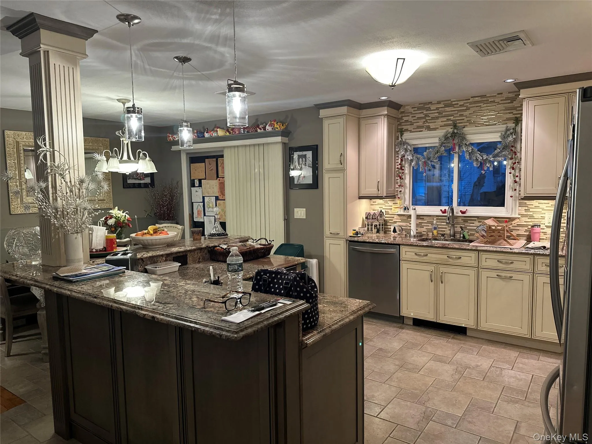 Kitchen with dark stone counters, decorative light fixtures, appliances with stainless steel finishes, cream cabinetry, and tasteful backsplash Kitchen with dark stone counters, decorative light fixtures, appliances with stainless steel finishes, cream cabinetry, and tasteful backsplash