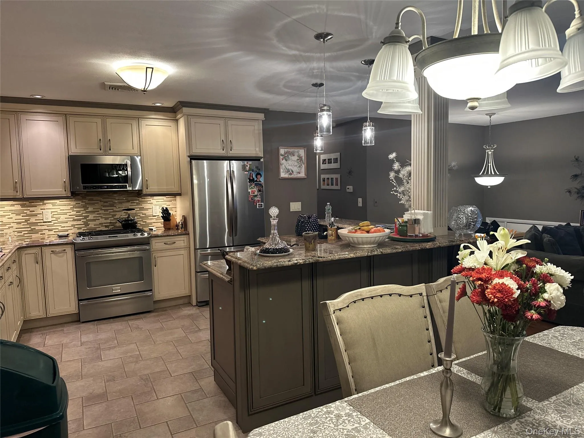 Kitchen featuring stainless steel appliances, dark stone countertops, decorative light fixtures, decorative backsplash, and cream cabinets Kitchen featuring stainless steel appliances, dark stone countertops, decorative light fixtures, decorative backsplash, and cream cabinets