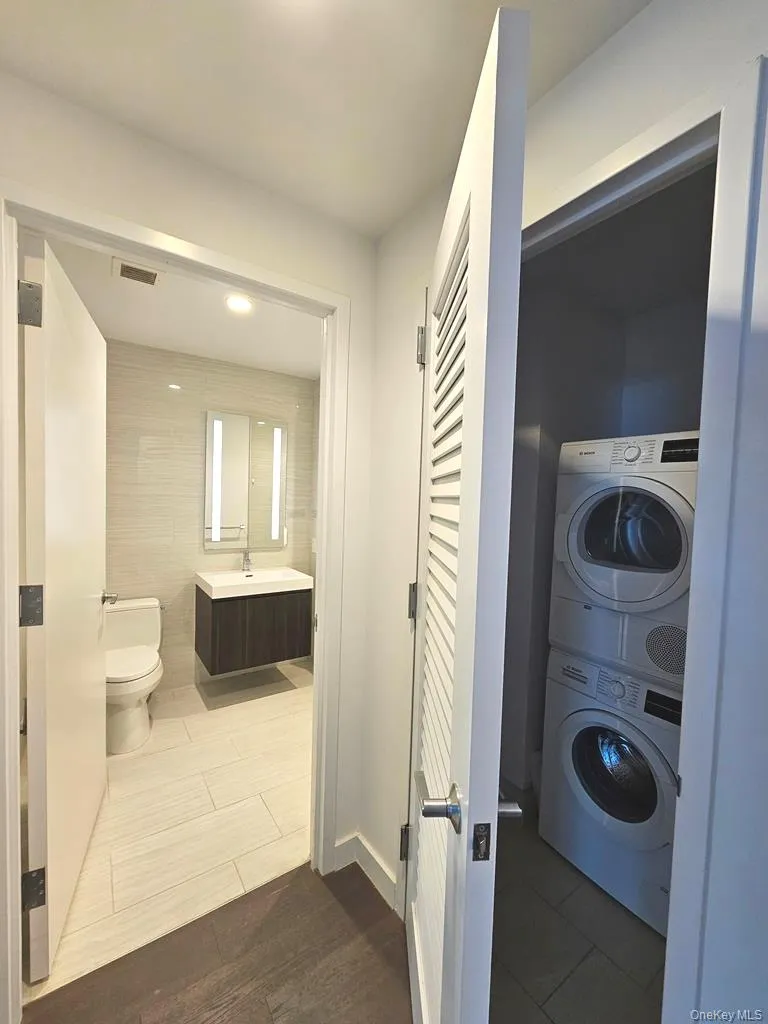 Washroom with stacked washer / drying machine, tile walls, and dark tile patterned flooring Washroom with stacked washer / drying machine, tile walls, and dark tile patterned flooring