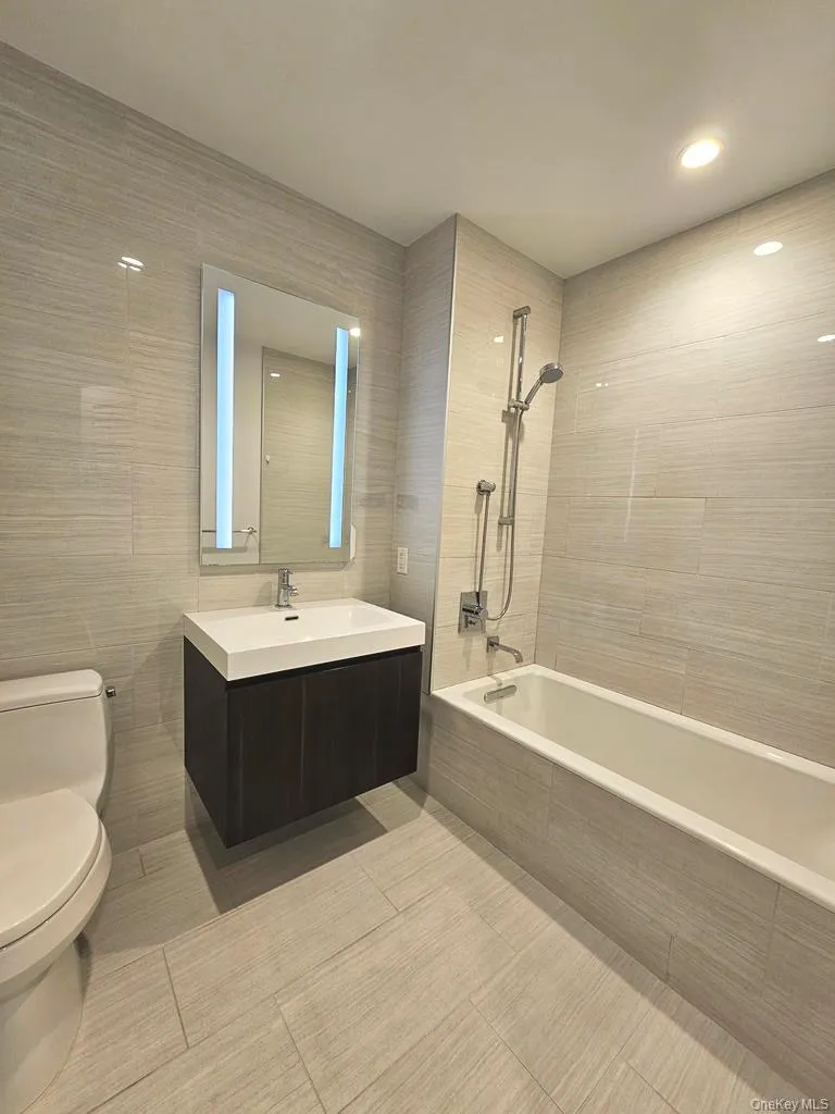 Bathroom with vanity, tiled shower / bath combo, tile walls, light tile patterned floors, and recessed lighting Bathroom with vanity, tiled shower / bath combo, tile walls, light tile patterned floors, and recessed lighting