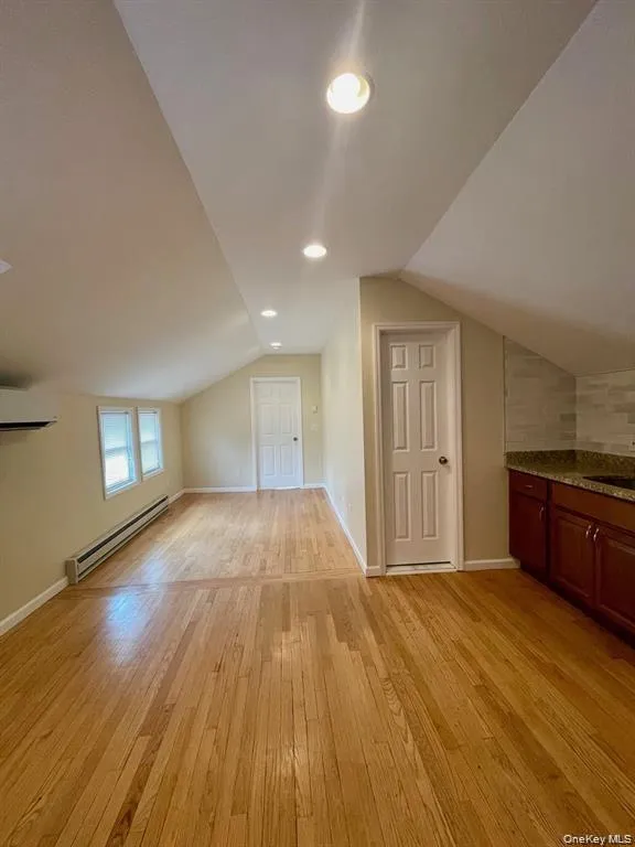 Additional living space with vaulted ceiling, a baseboard radiator, light wood-type flooring, recessed lighting, and a wall mounted AC Additional living space with vaulted ceiling, a baseboard radiator, light wood-type flooring, recessed lighting, and a wall mounted AC