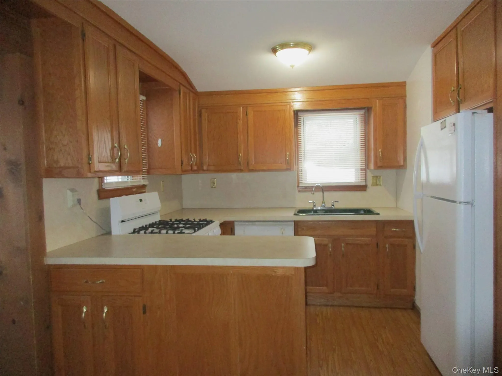 Kitchen with white appliances, light countertops, a peninsula, light wood-style flooring, and light brown cabinetry. Natural gas stove/oven. Kitchen with white appliances, light countertops, a peninsula, light wood-style flooring, and light brown cabinetry. Natural gas stove/oven.