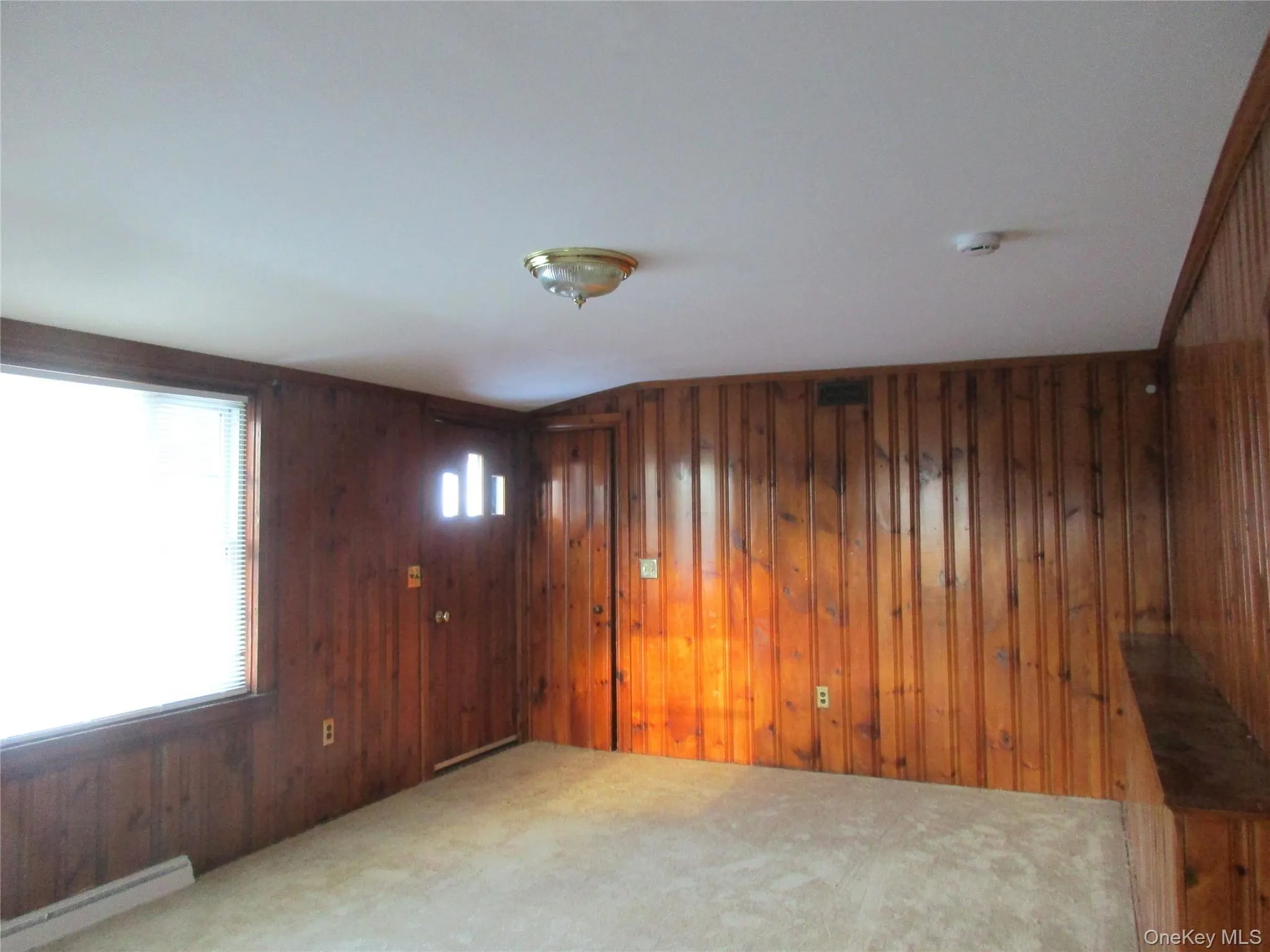 Carpeted living room, original wood walls, picture window, door to deck, and baseboard heating Carpeted living room, original wood walls, picture window, door to deck, and baseboard heating